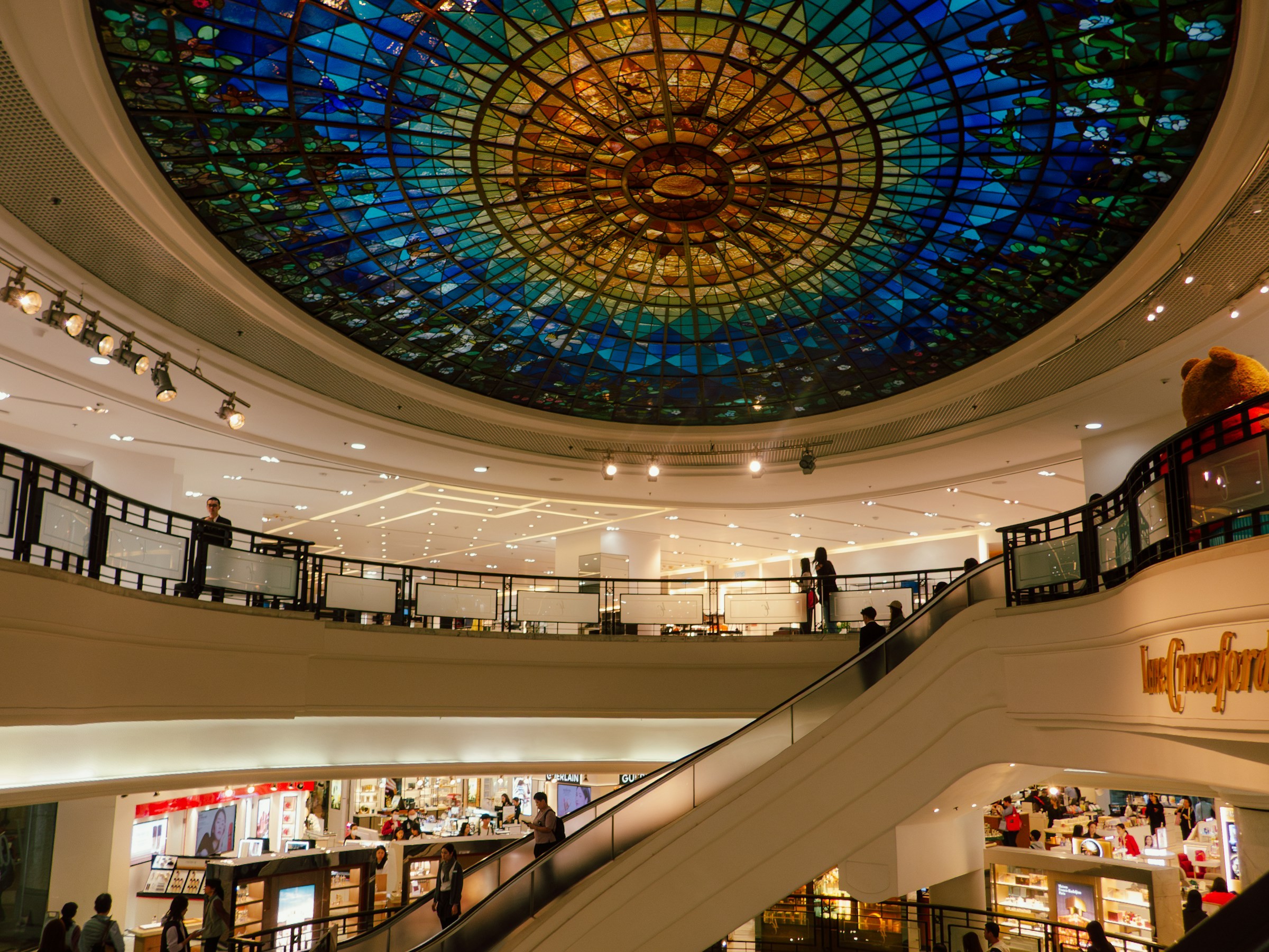 A grand shopping mall atrium beneath a colorful stained-glass dome